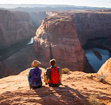 Two people sitting on a plateau overlooking a canyon.