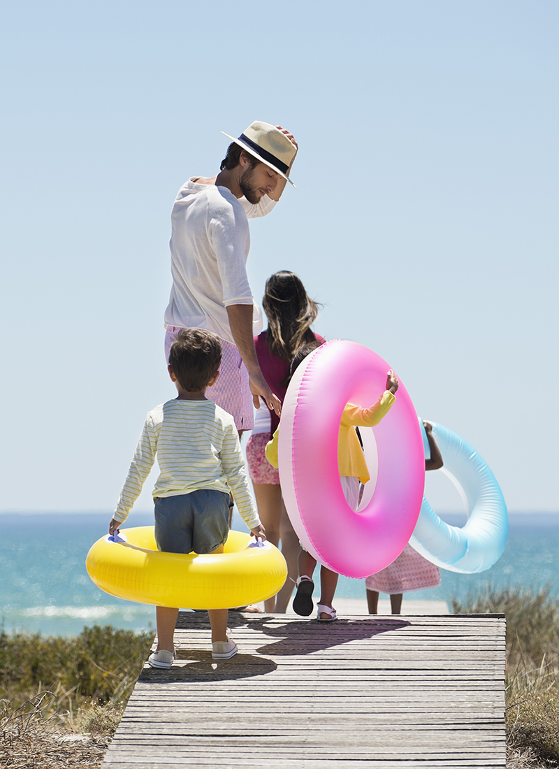 Man with kids heading to the beach with colorful tubes